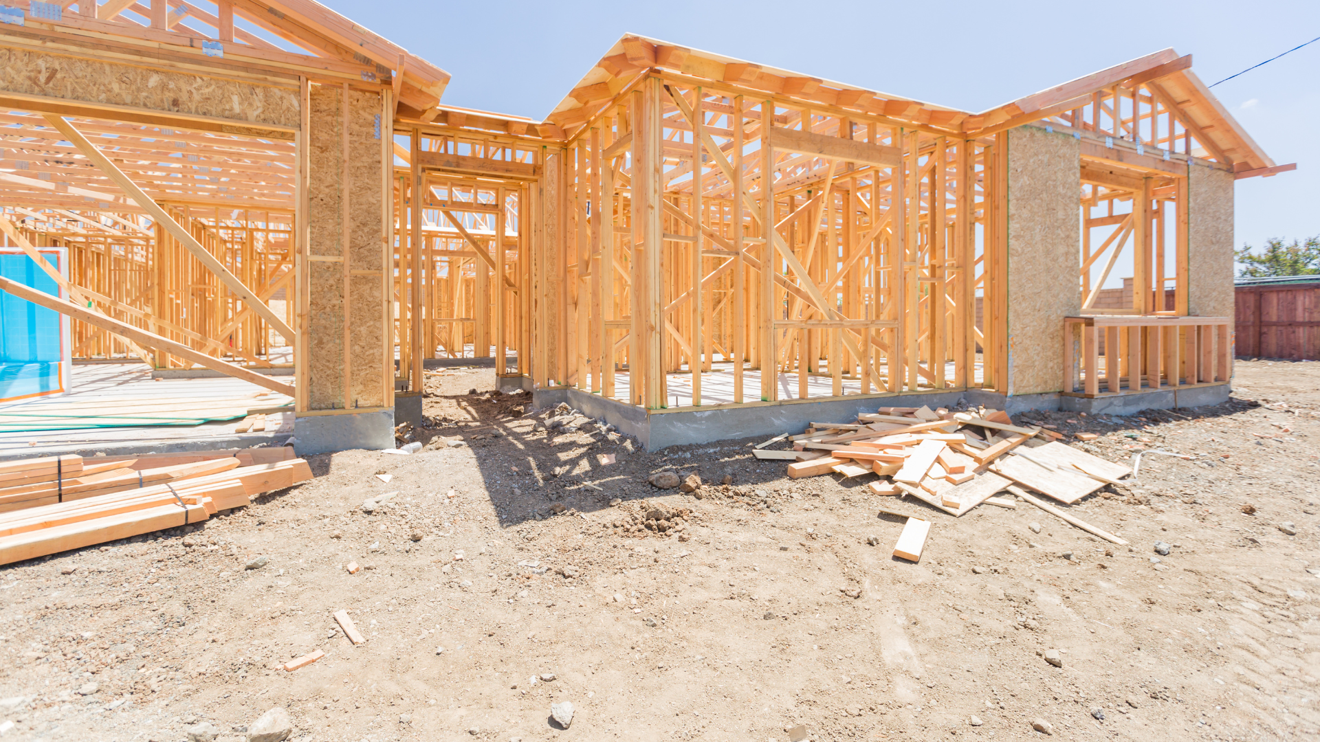 Wooden framework of a house under construction, on a dirt lot, sunny day.