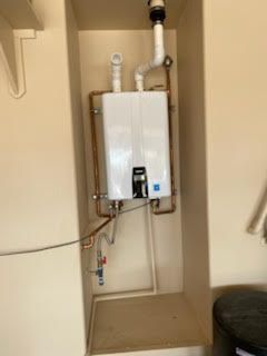 White tankless water heater installed in a recessed wall area with copper pipes.