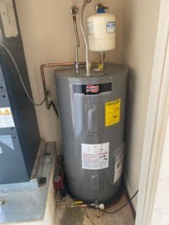 Water heater in a utility closet with pipes and an expansion tank.