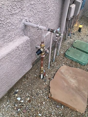 Outdoor plumbing against a stucco wall, with valves and copper pipes visible.
