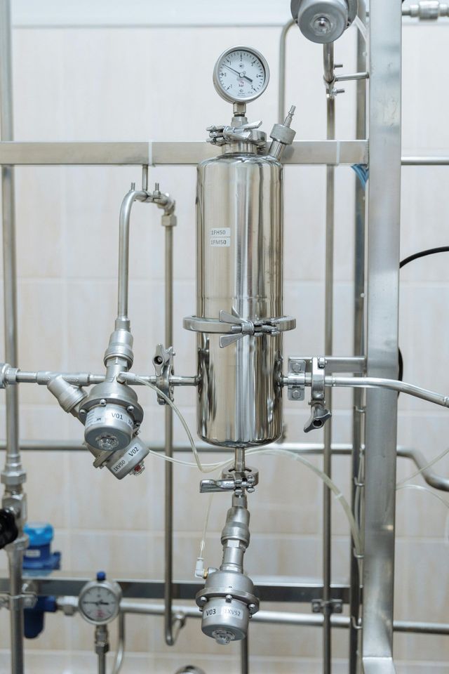 Stainless steel industrial equipment with gauges and pipes in a white-tiled room.
