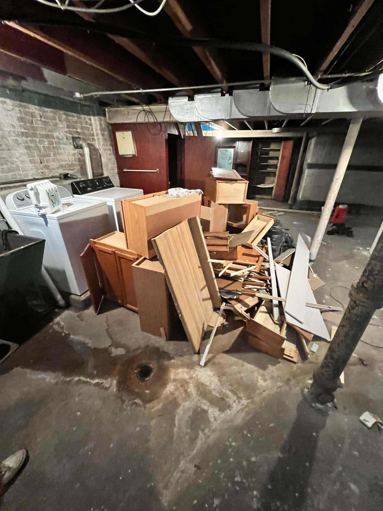 Cluttered basement with discarded furniture and debris piled on the concrete floor. Walls and ceiling are unfinished.