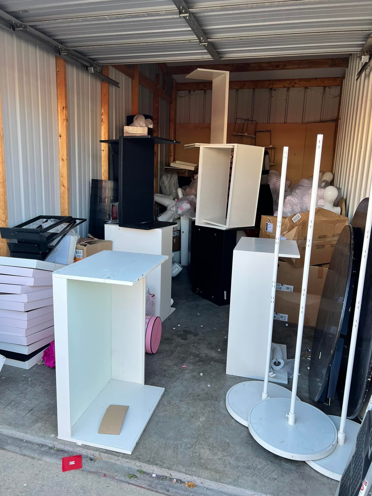 Storage unit filled with white and black furniture, boxes, and displays. A garment rack stands at the right.