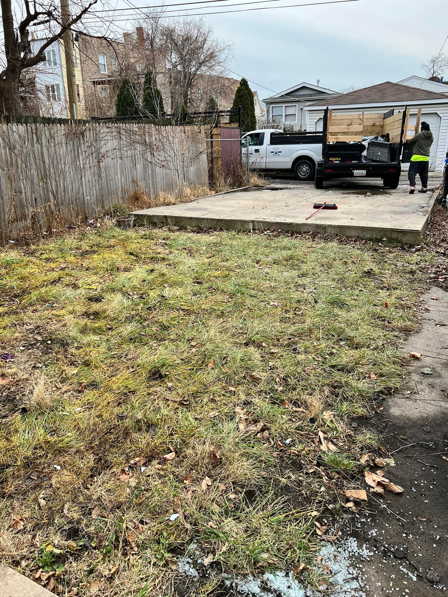 Yard with overgrown vegetation; two trucks and two people are visible in the background.