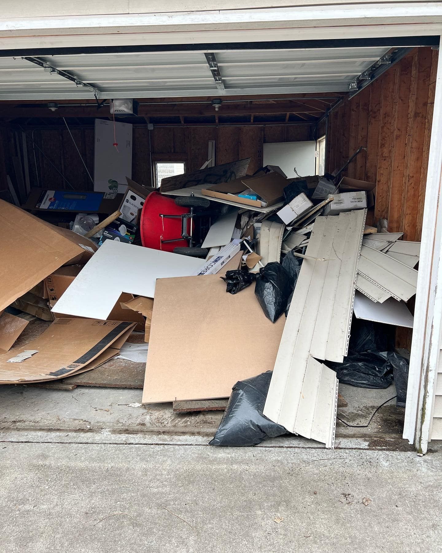 Open garage filled with a large pile of discarded items, including cardboard, wood, and a red drum.