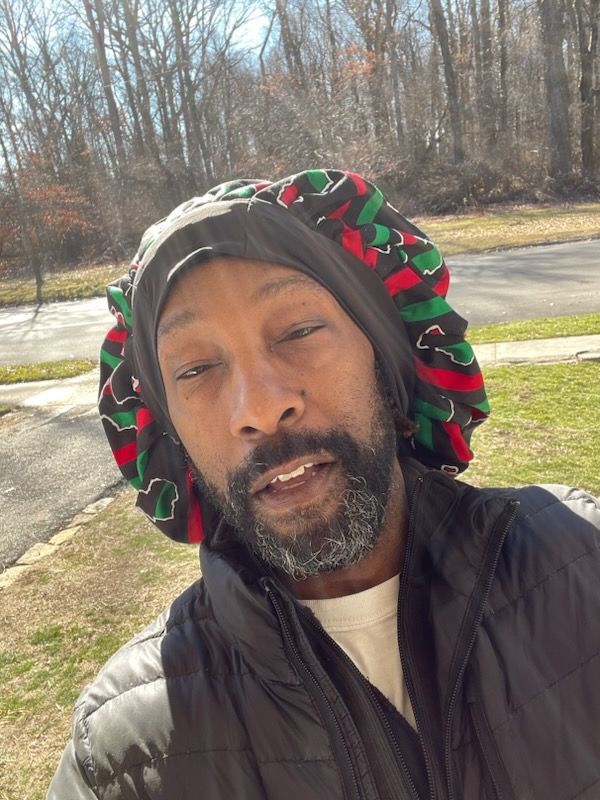 A man with a beard is wearing a bonnet and a jacket.