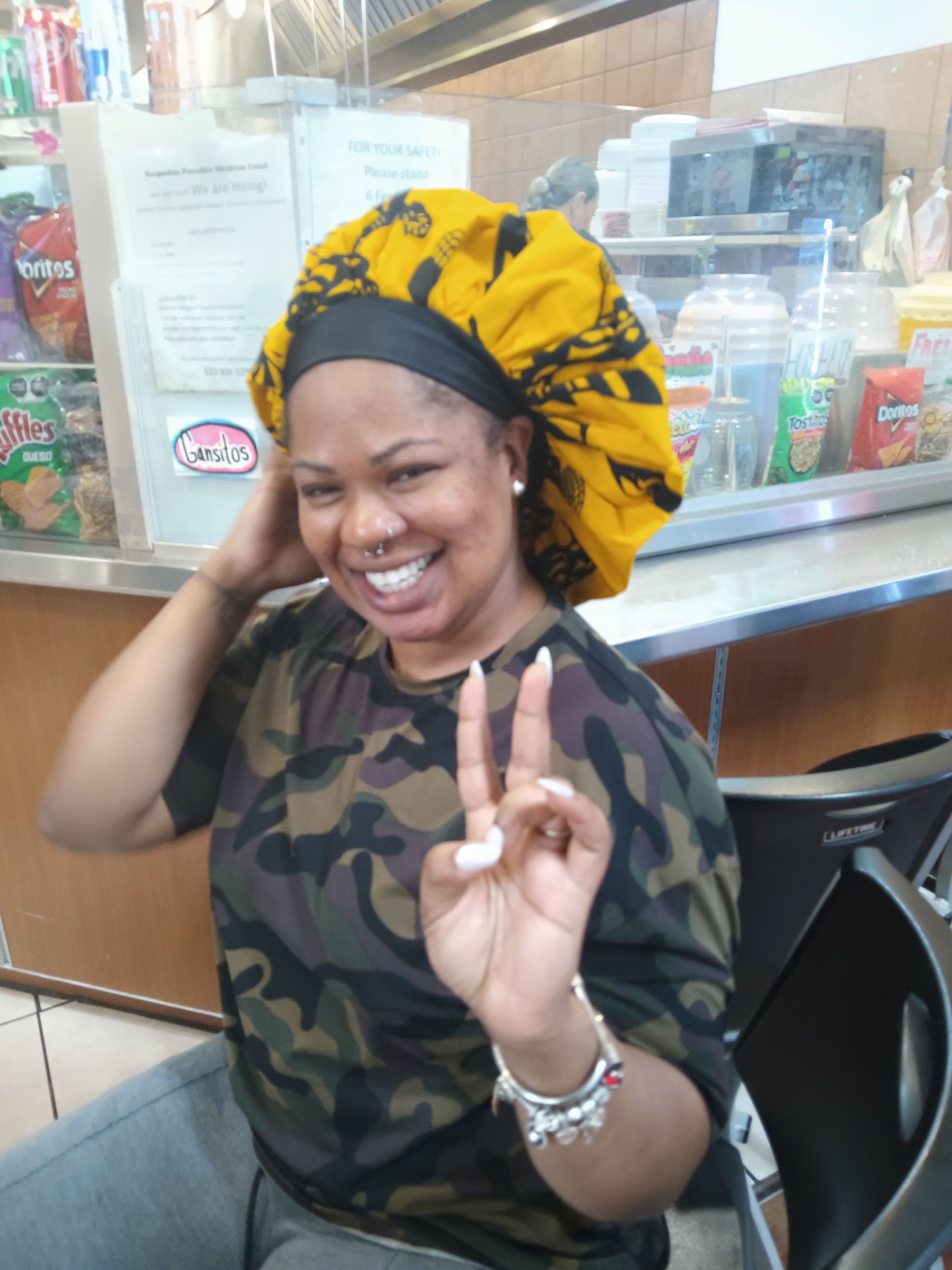 A woman wearing a camouflage shirt and a yellow  bonnet  is giving a peace sign.