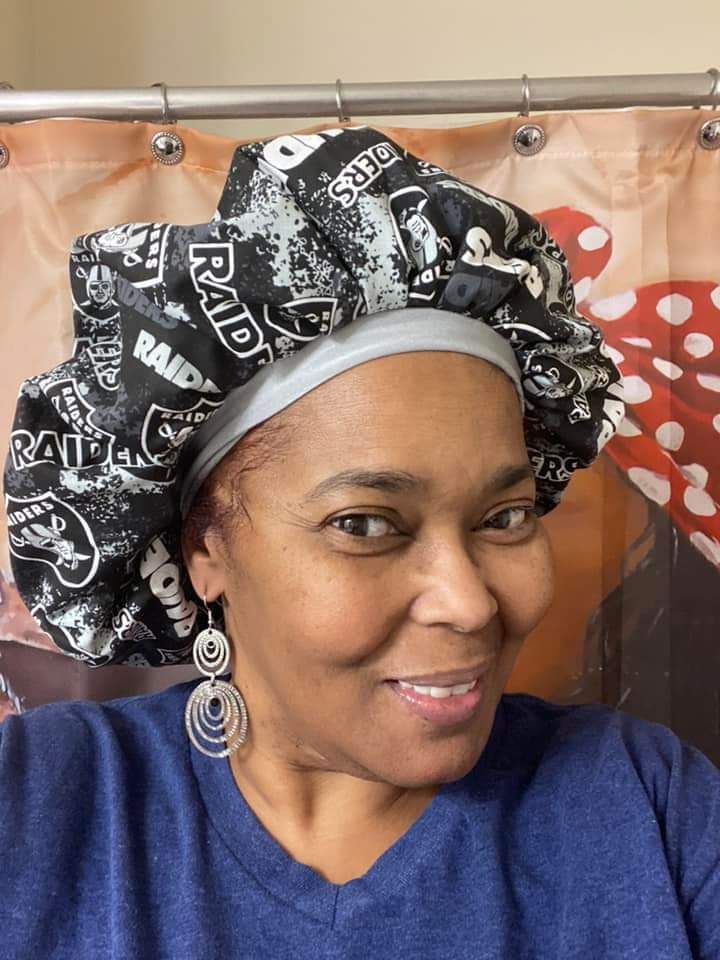 A woman wearing a raiders bonnet and earrings is smiling in front of a shower curtain.
