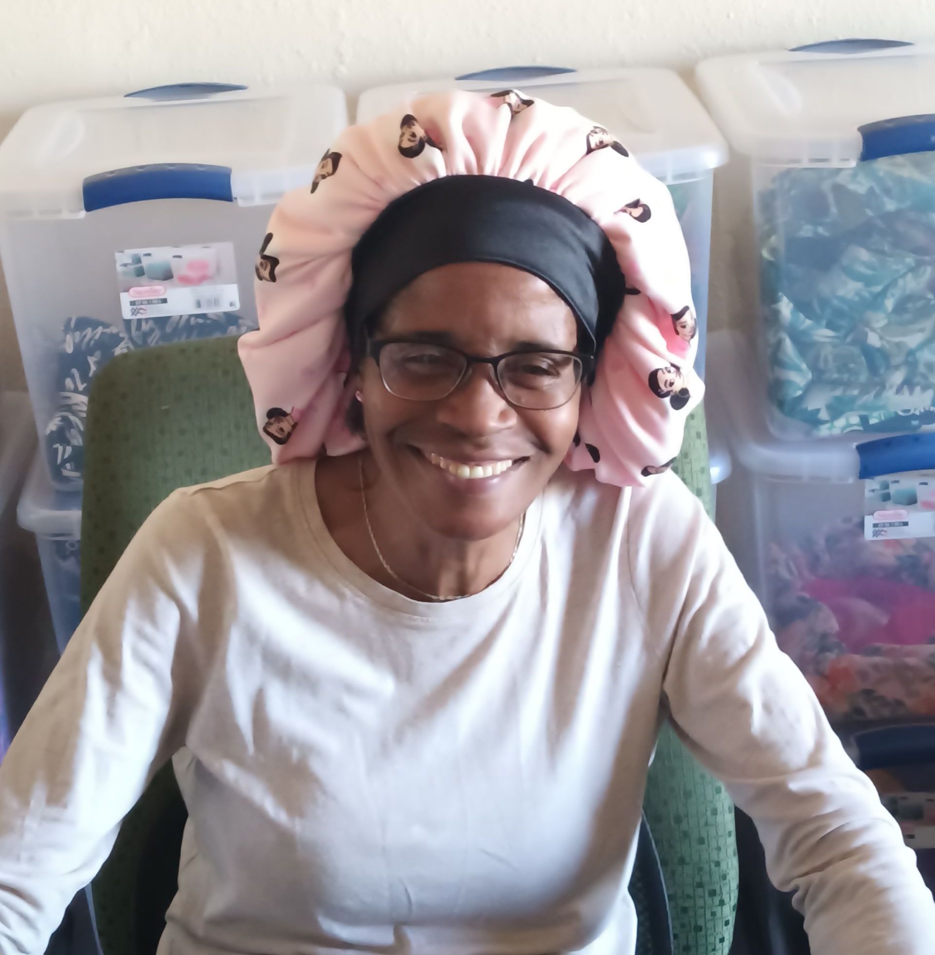 A woman wearing glasses and a pink bonnet  is smiling