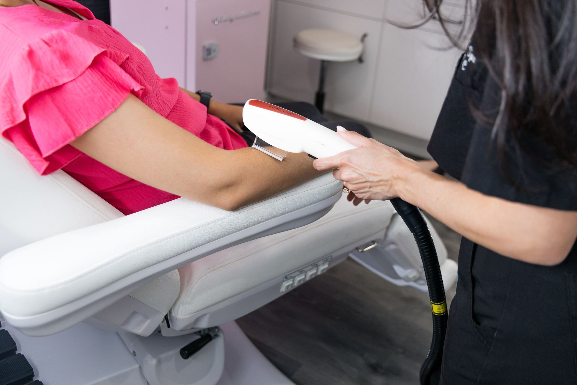 A woman in a pink shirt is getting a laser treatment on her arm