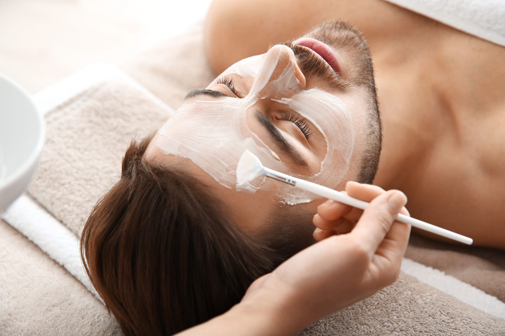 A woman wearing a mask and pink gloves is examining a woman's face