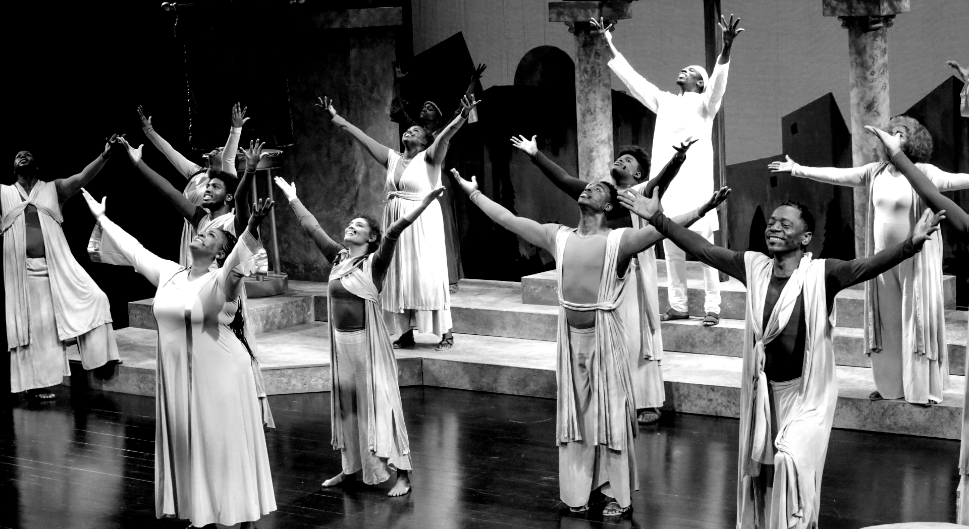 Group of people with arms raised in performance. Black and white photo.