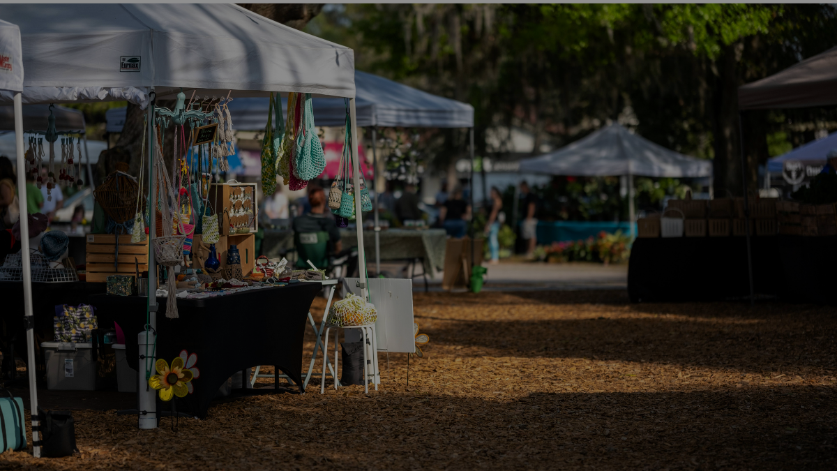 Outdoor artisan market with tents, tables, and vendors selling goods on a sunny day.