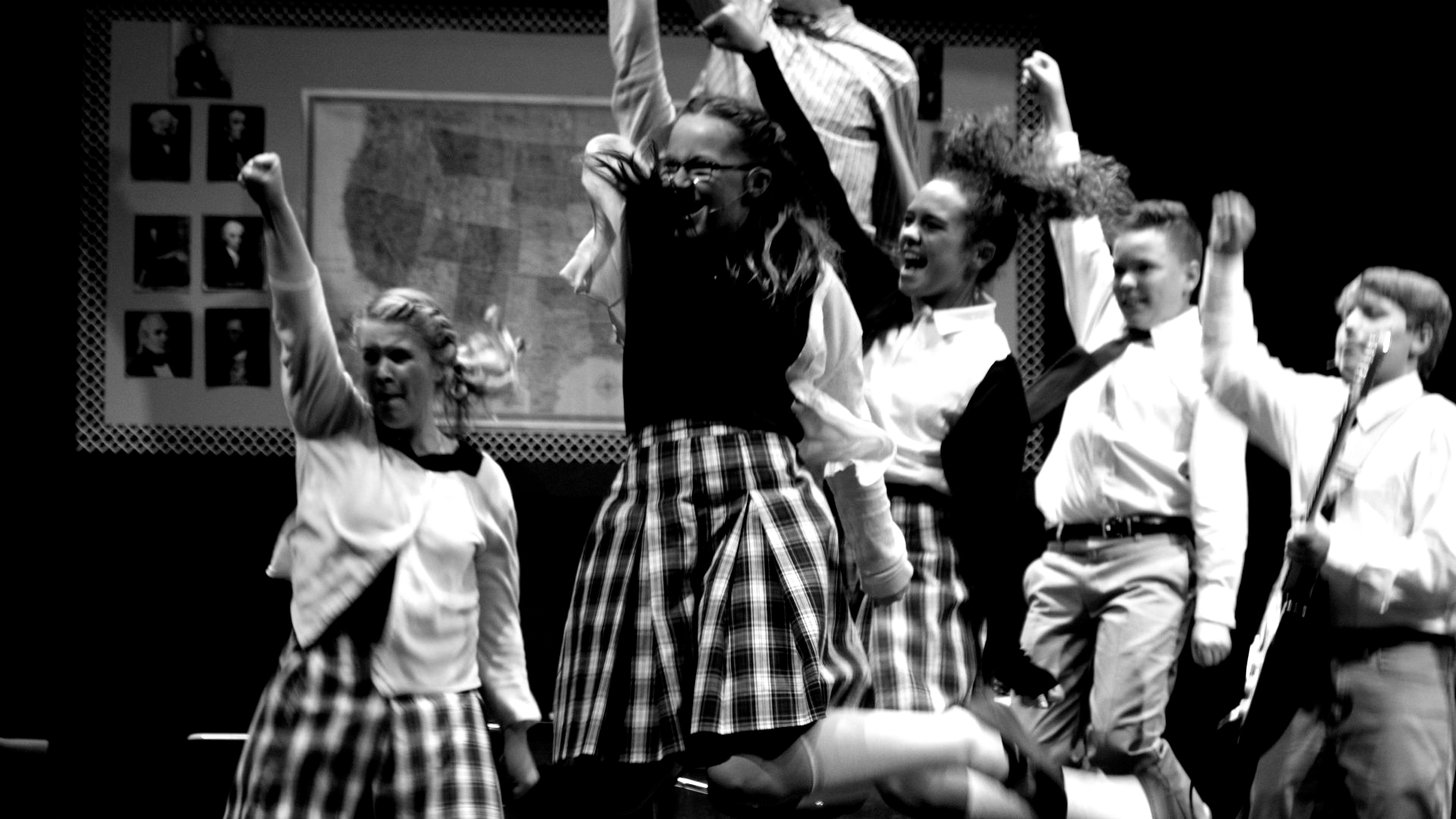 Group of students in school uniforms cheering on stage.