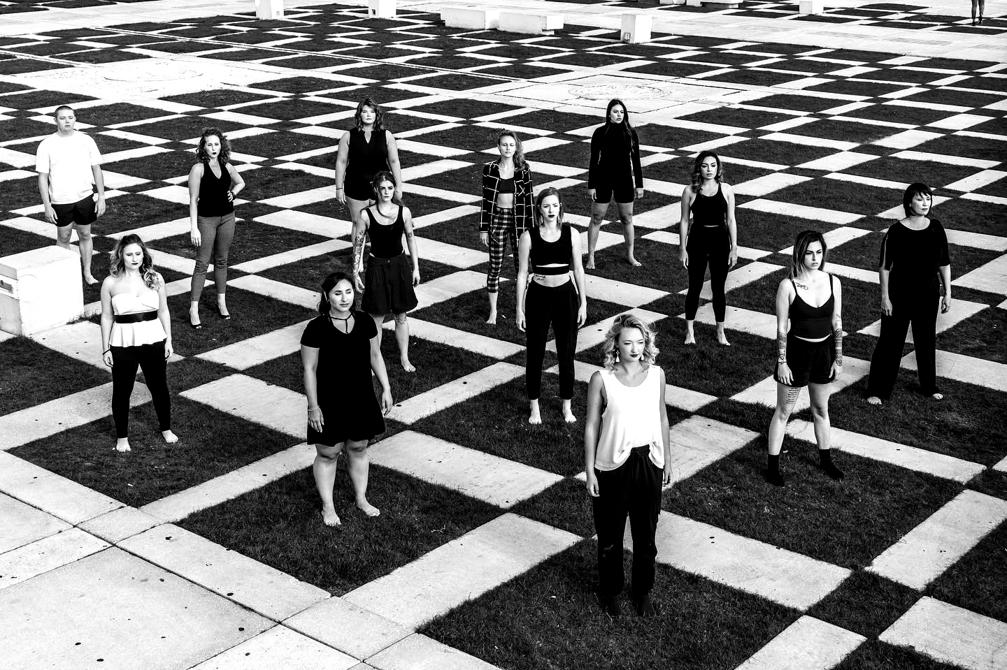 Group of people standing on a black and white checkered surface. Mostly women. Outdoor setting.
