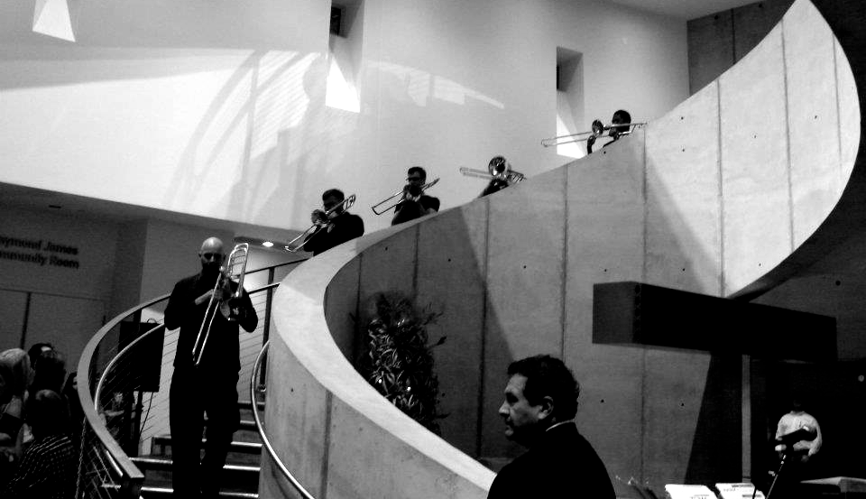 A trombone player descends stairs, leading a jazz band on a curved wall.