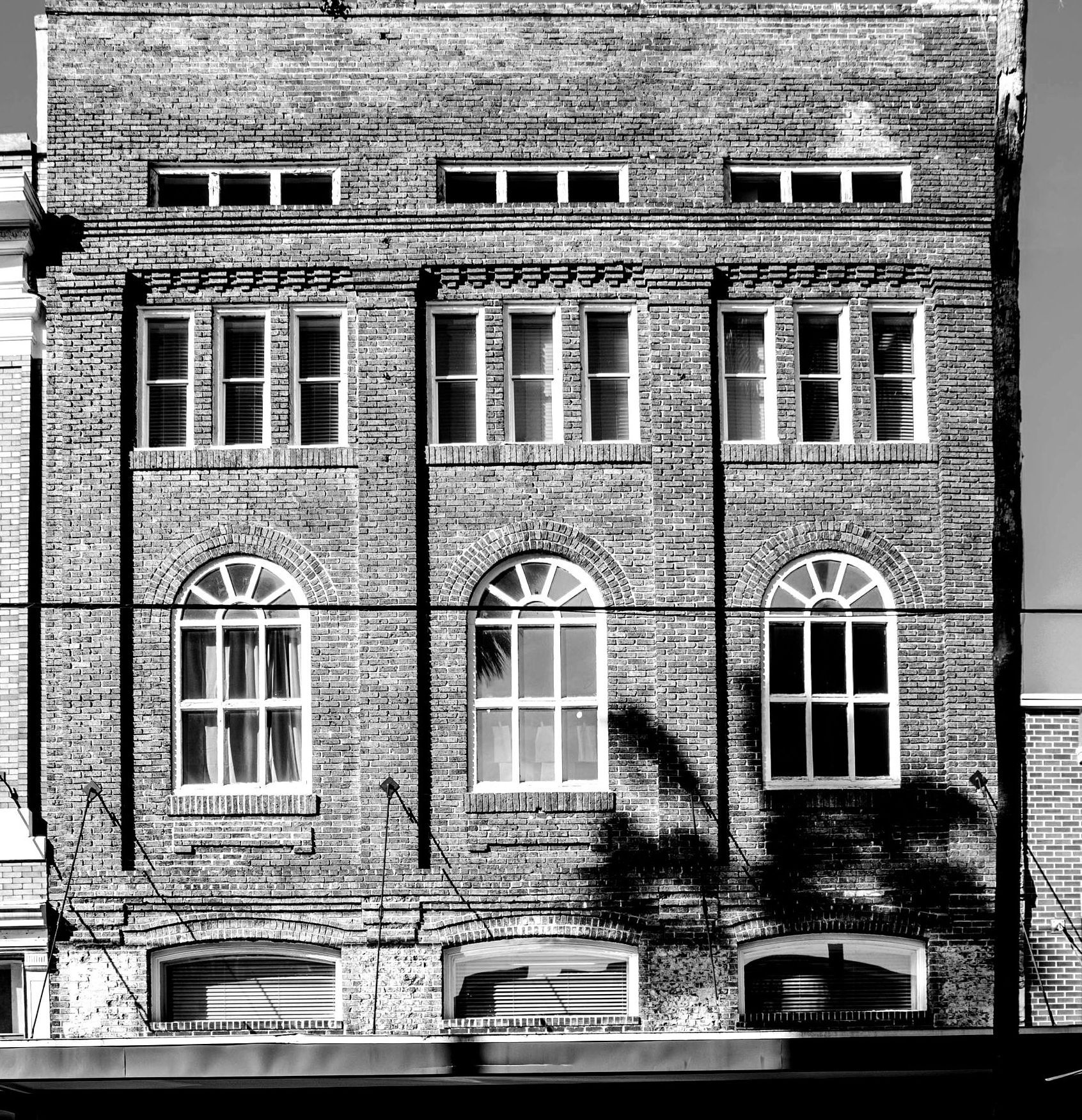 Brick building facade with arched and rectangular windows; black and white.