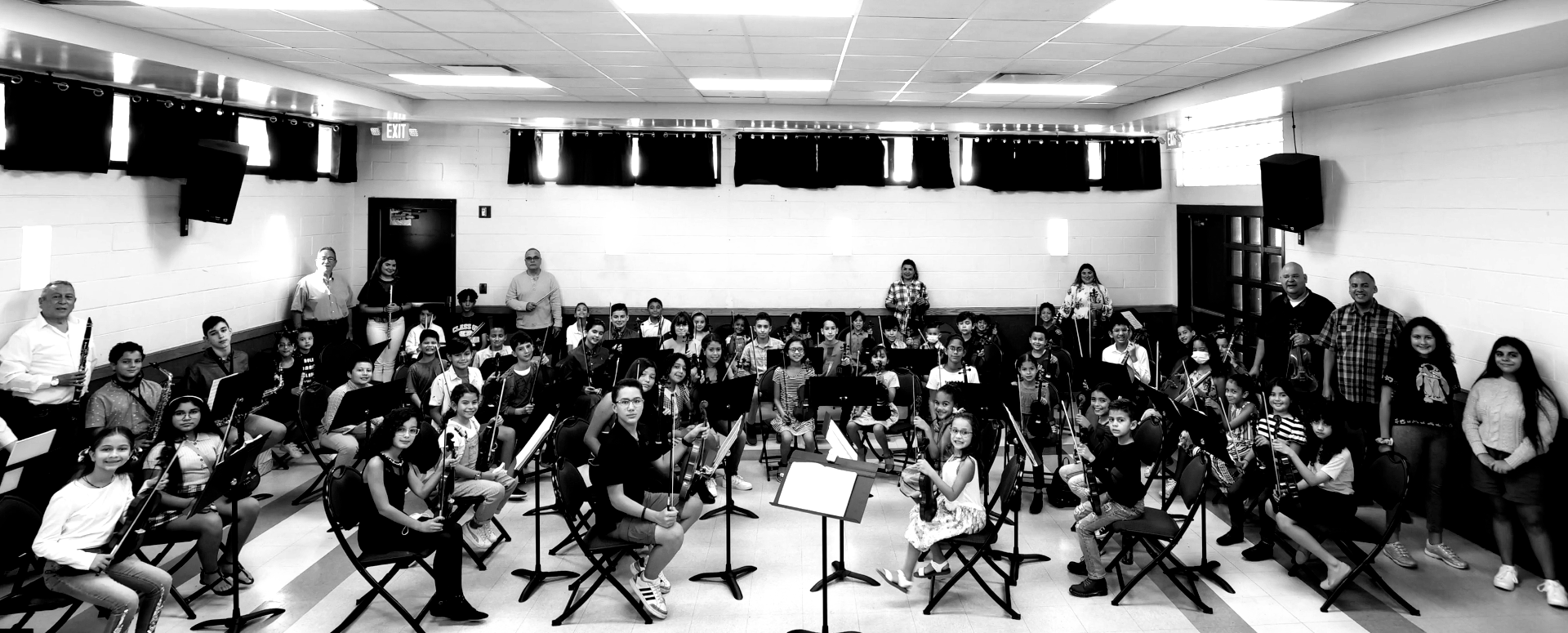 A large group of people, likely a band or orchestra, gathered in a classroom.