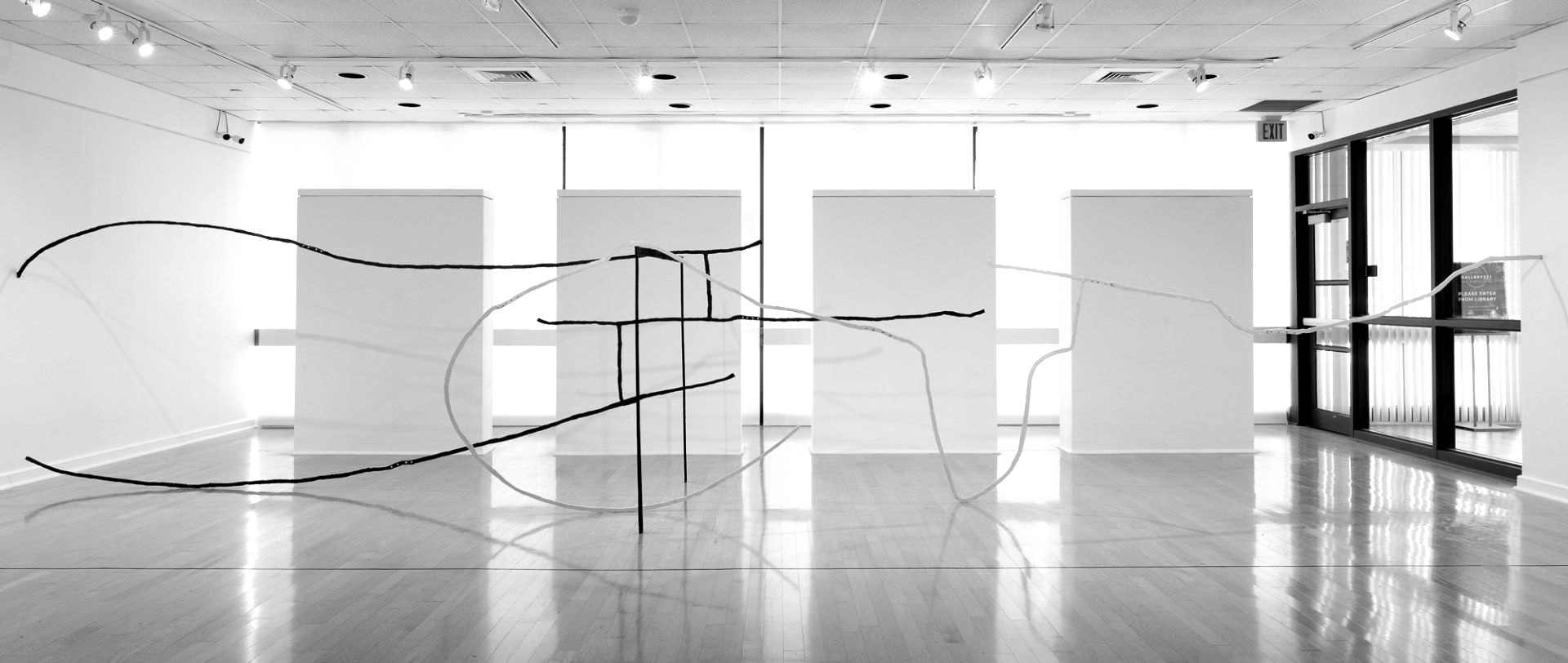 A gallery interior featuring a black-and-white art installation with intersecting lines and blank panels.