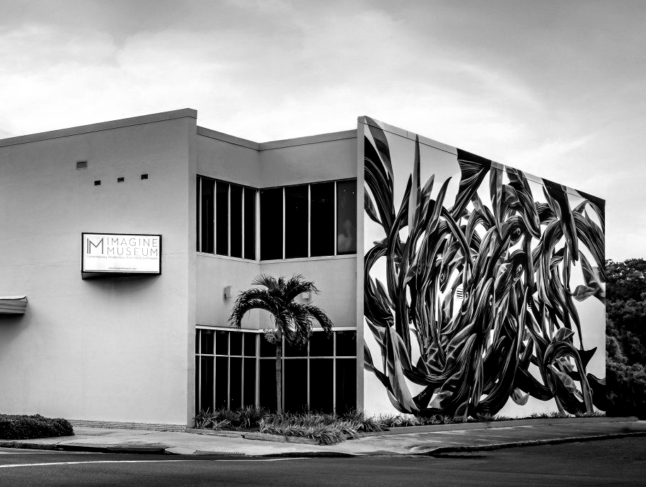 Black and white photo of a building with a large mural of plants on one wall. The sign reads 