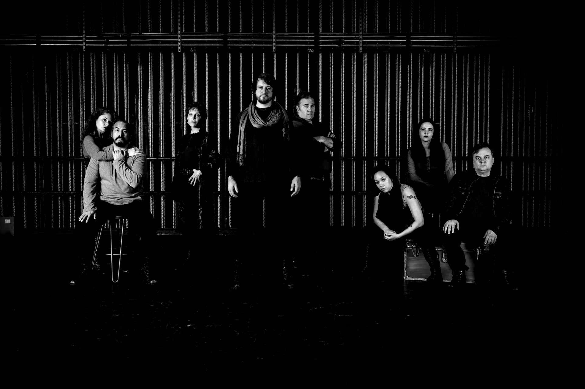 Group of diverse people in dark clothing in front of a metal panel backdrop.