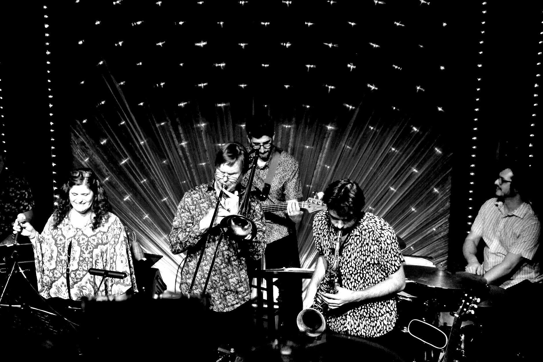 Band of five musicians performing on stage under a spotlight.