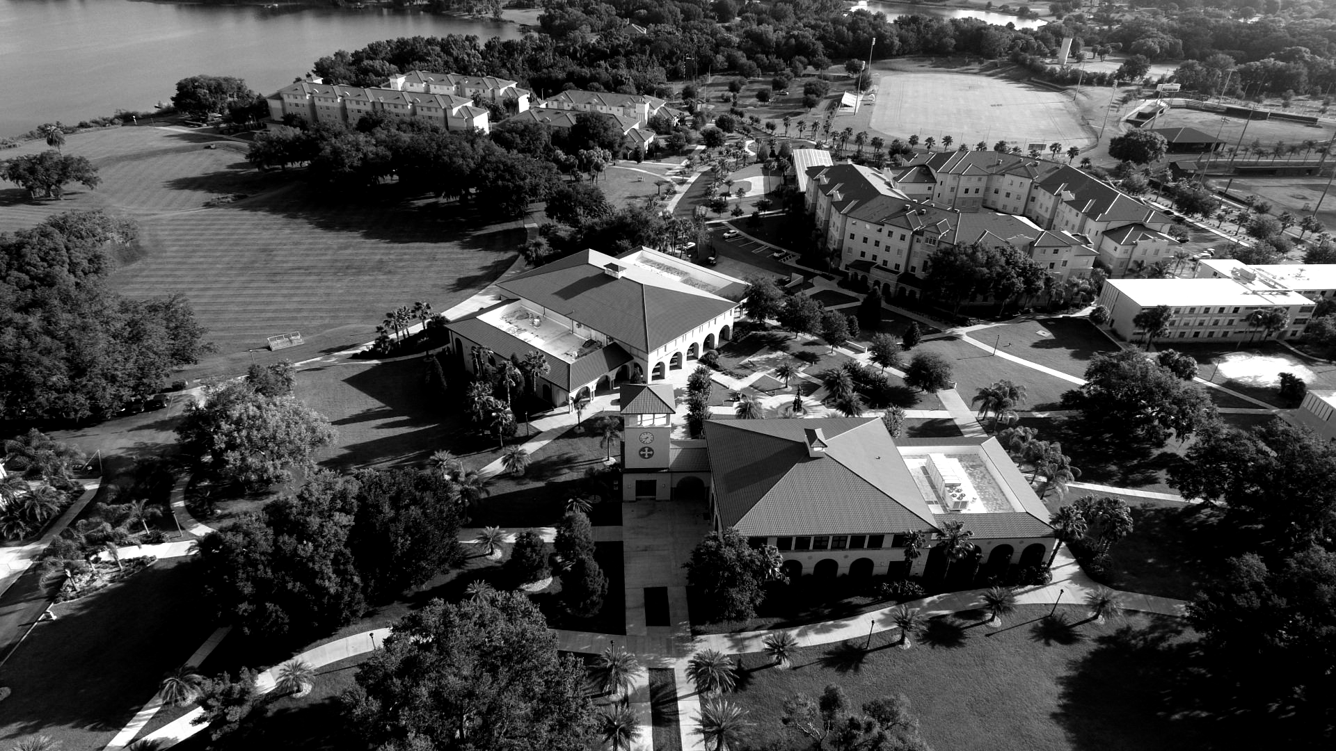 Aerial view of a campus with buildings, green space, and a body of water in the background.