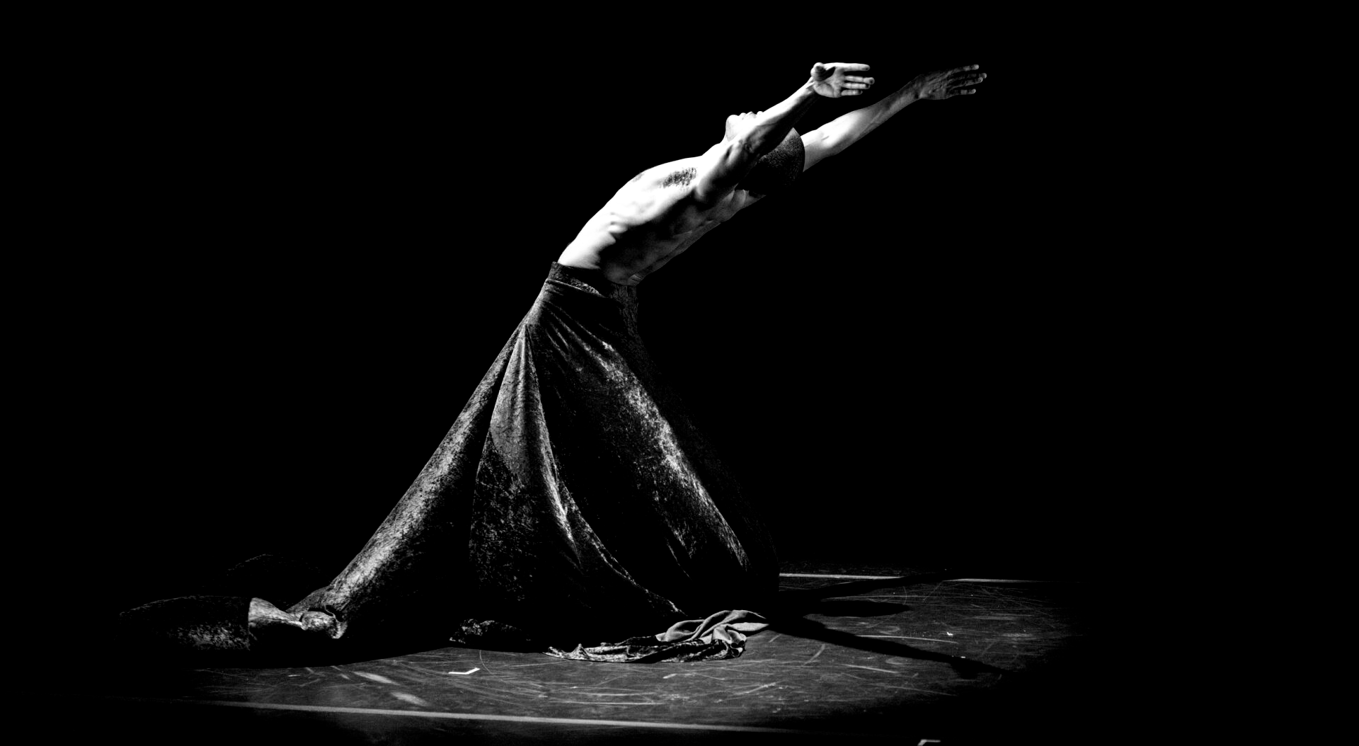 A figure arches back dramatically on a stage, arms outstretched, in black and white.