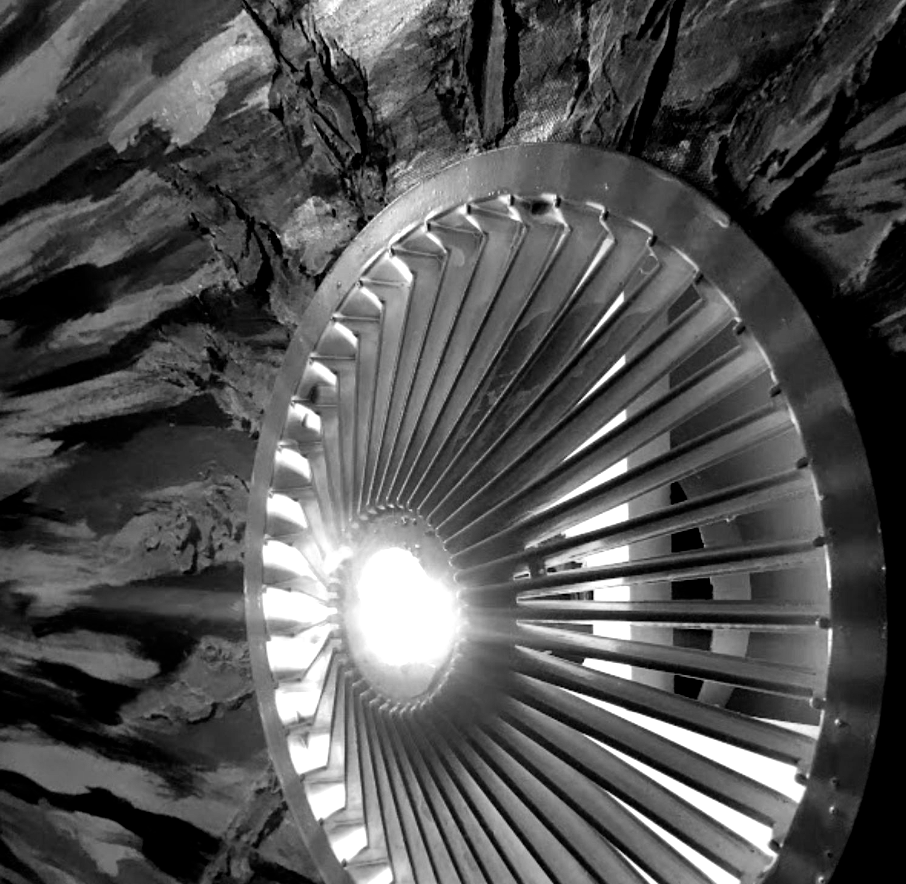 Metal turbine fan in front of a textured, dark background, likely an industrial setting.