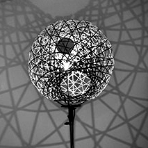 Black and white photo of a spherical lamp, casting web-like shadows on a wall.