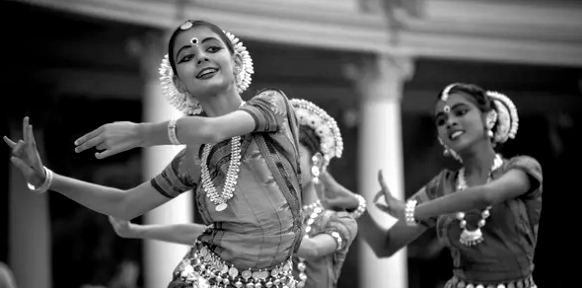 Two Indian dancers in traditional dress, performing with expressive hand gestures and smiles.