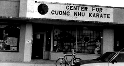 Center for Cuong Nhu Karate storefront with yin-yang symbol, bicycle, and car; a person is visible inside.
