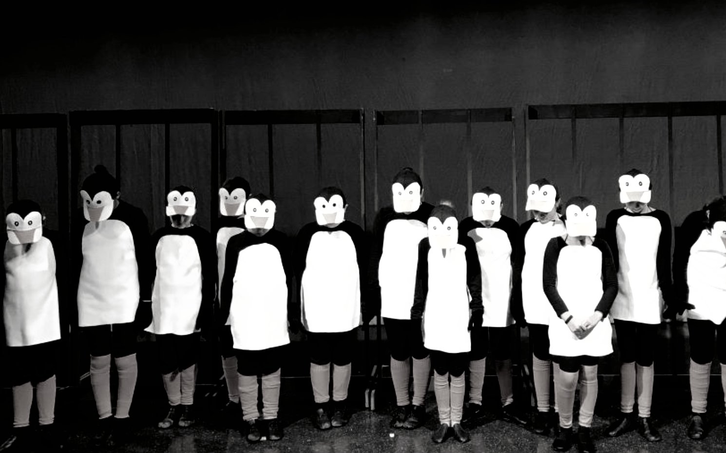Group of children in penguin costumes posing in front of a dark backdrop. Black and white.
