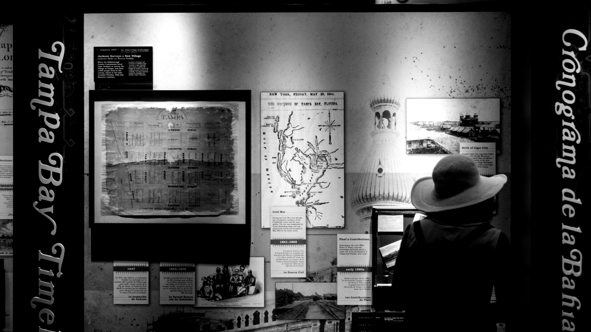 Person in a hat looking at vintage maps and photos on a wall. 