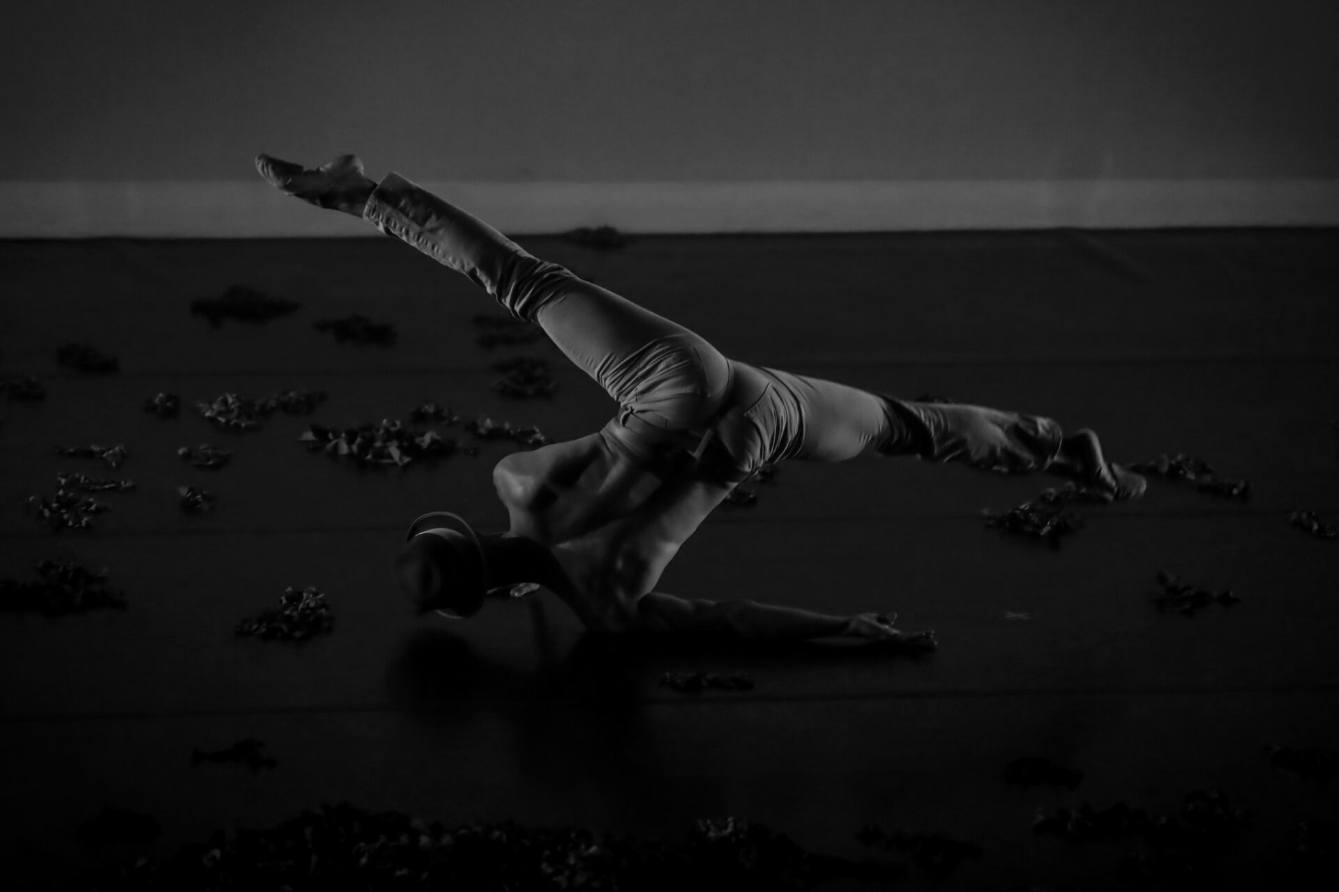Dancer performs a pose on the floor, back arched, leg extended upwards. Black and white.