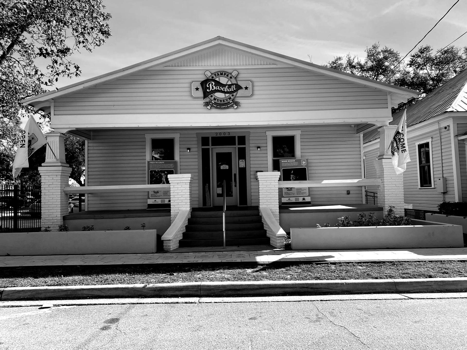 Black and white photo of a single-story building with a porch. A sign above the entrance reads 
