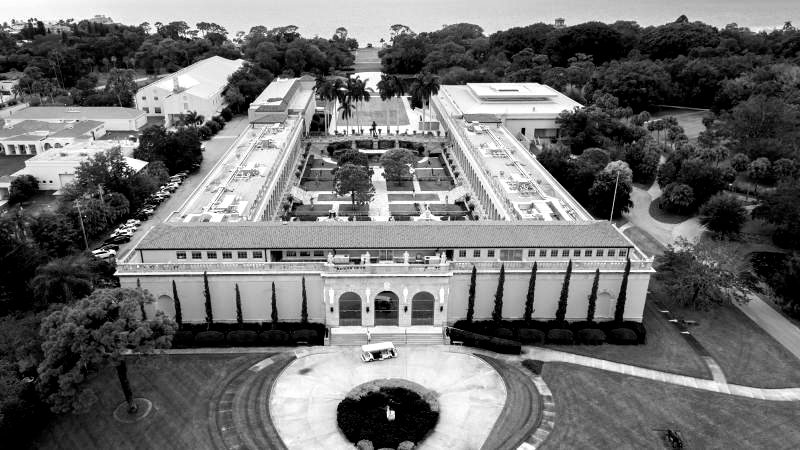 Black and white aerial view of a large U-shaped building with a garden courtyard, trees, and lawn.