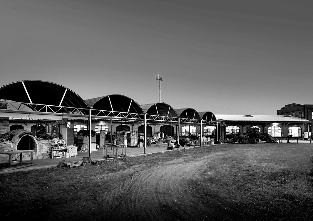 Black and white photo of a building with arched roofs. A dirt path leads to the entrance.