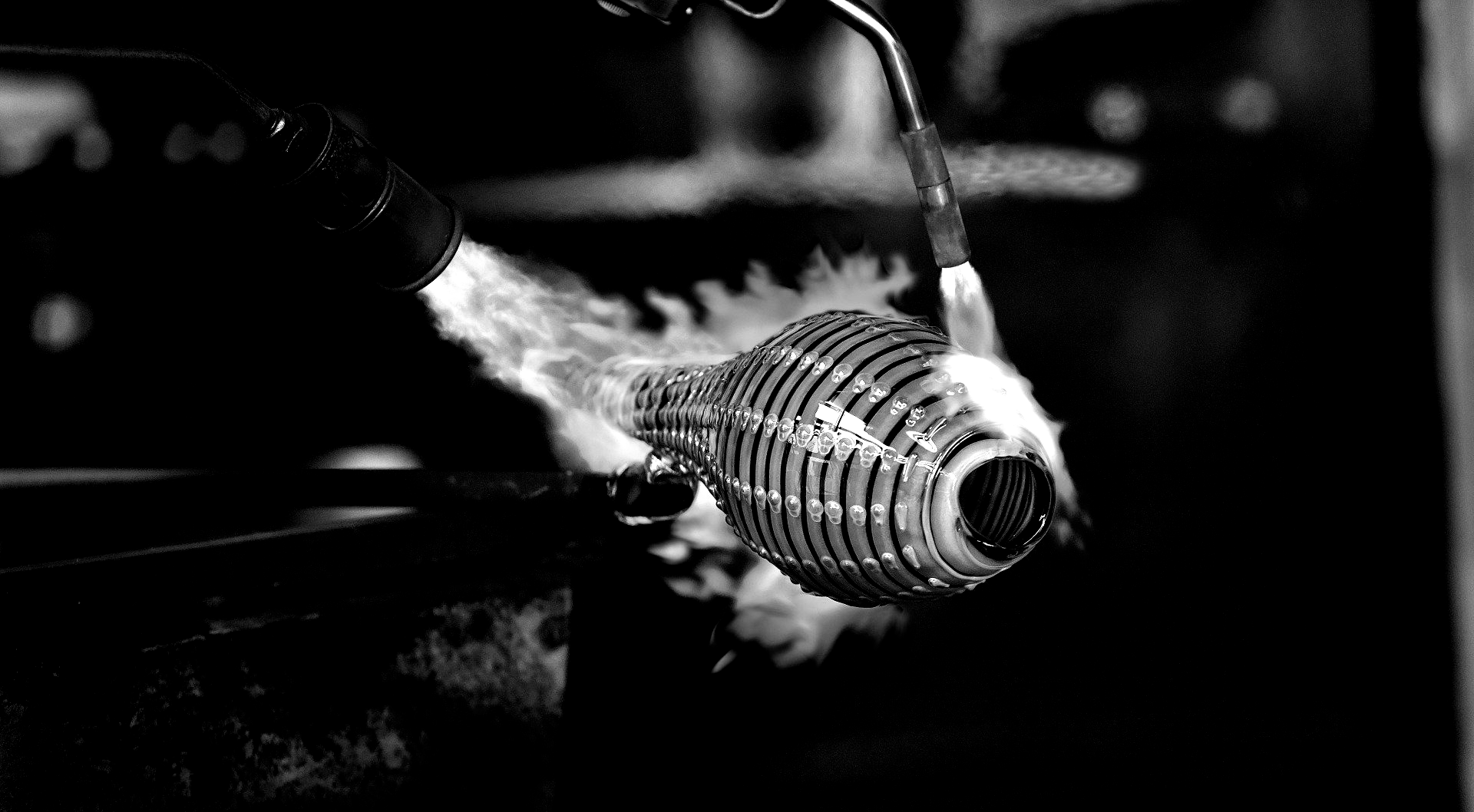 A glassblower heats a cylindrical glass form with a torch, creating vapor.