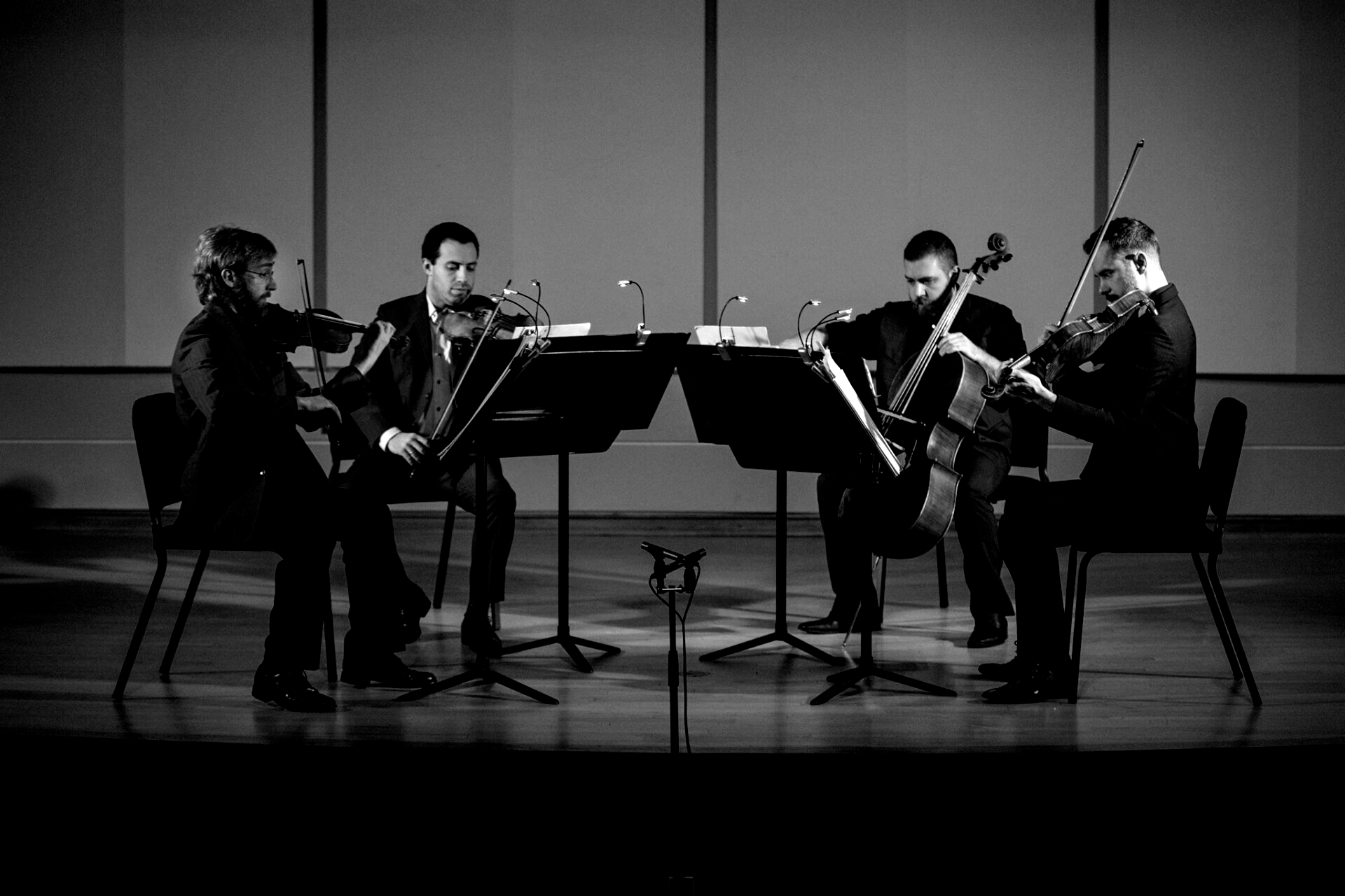 Black and white photo of a string quartet performing on stage, each musician seated and playing their instrument.