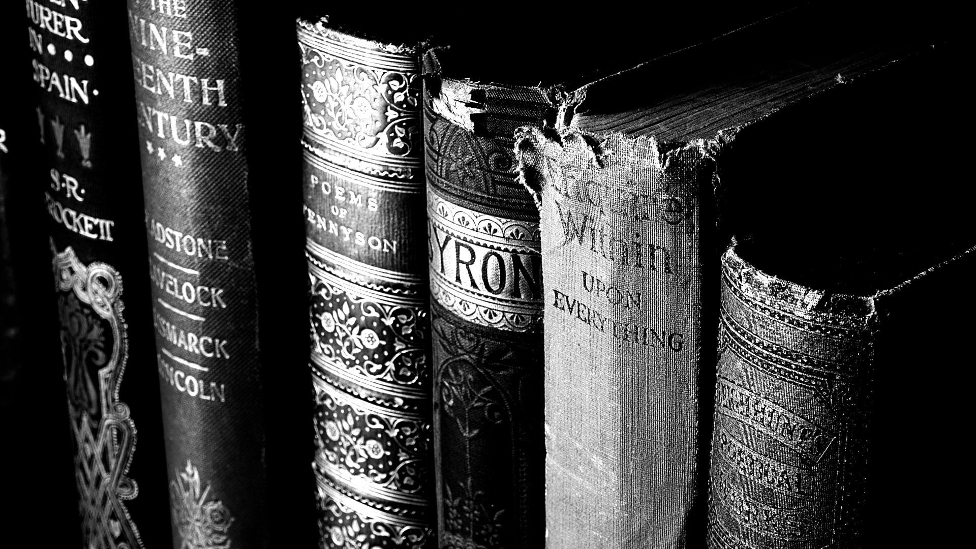 Black and white close-up of antique books on a shelf, spines visible with embossed titles and wear.