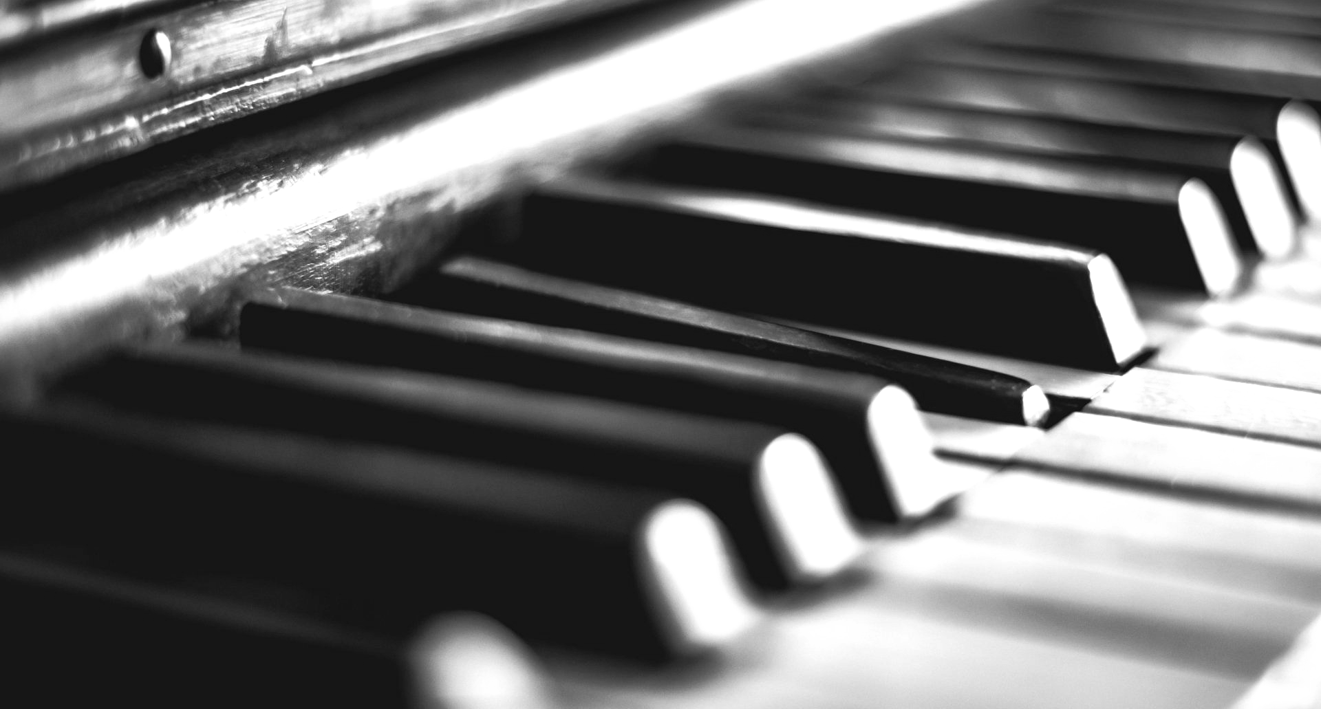 Piano keyboard, black and white, close-up perspective, showcasing keys and wood grain.