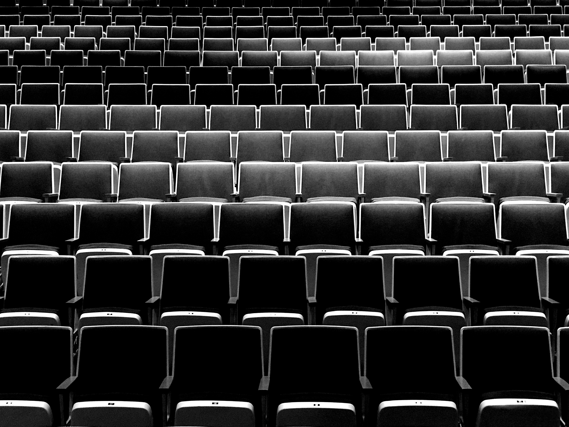 Rows of empty theater seats, a repetitive black and gray pattern.