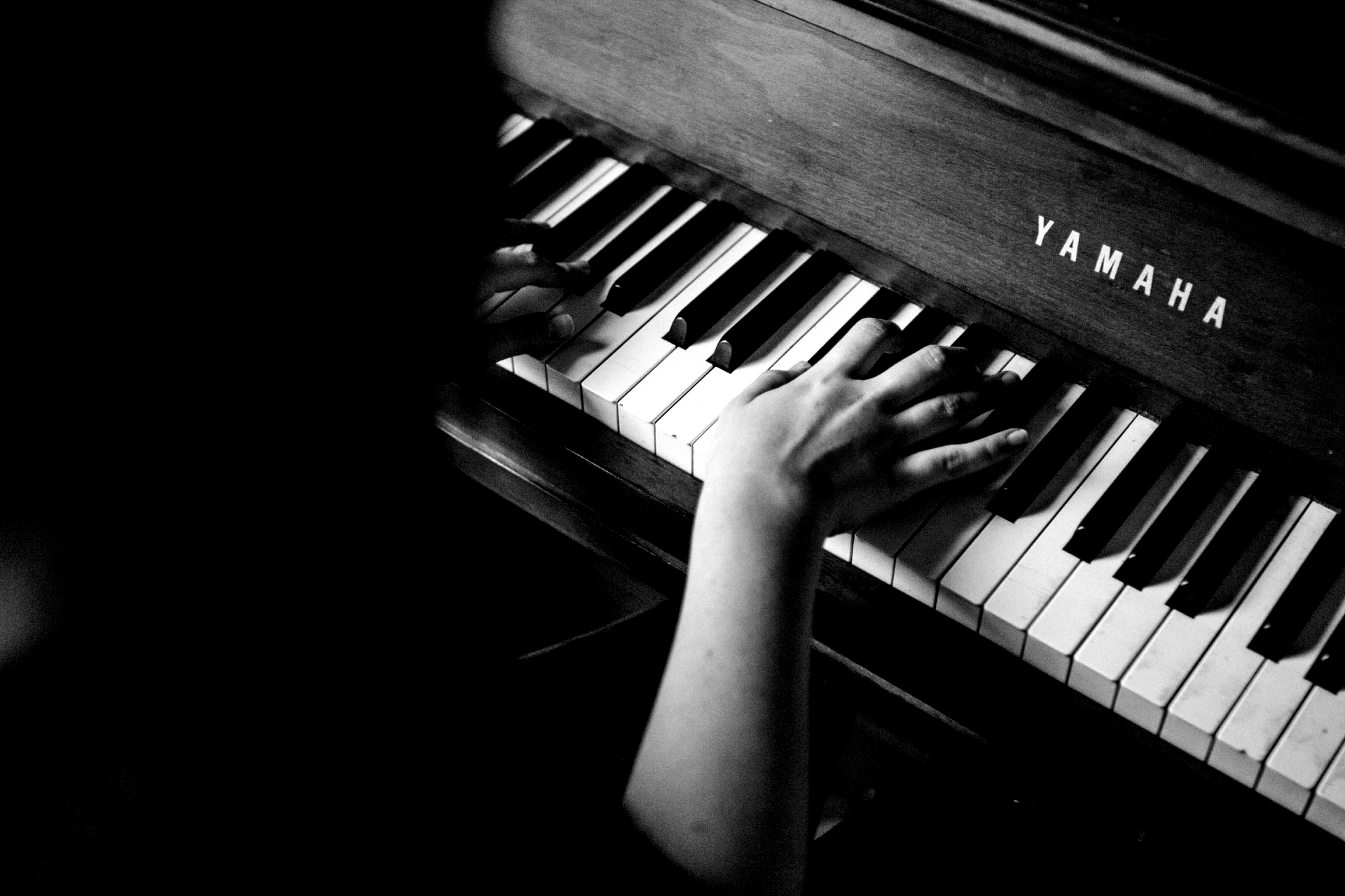 Hands playing a Yamaha piano, black and white.