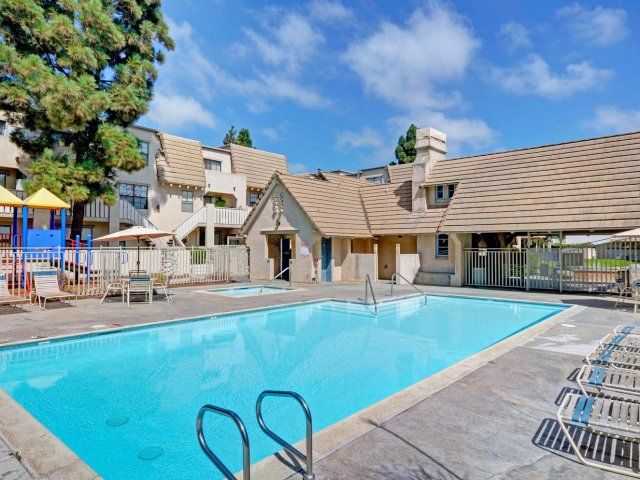 A large swimming pool is surrounded by chairs and umbrellas in front of a building.