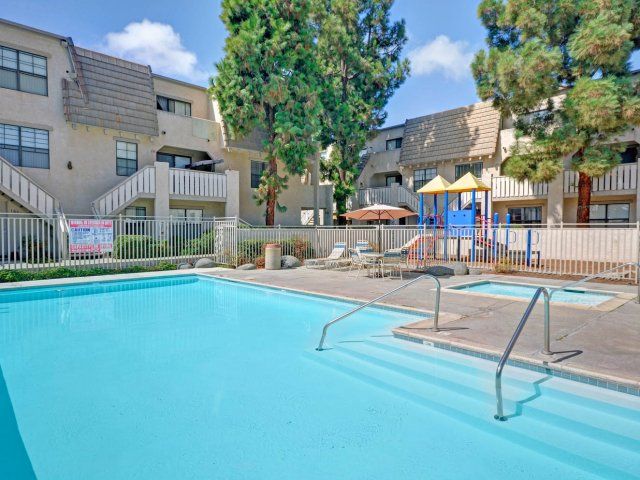 A large swimming pool in front of a building with a playground in the background.