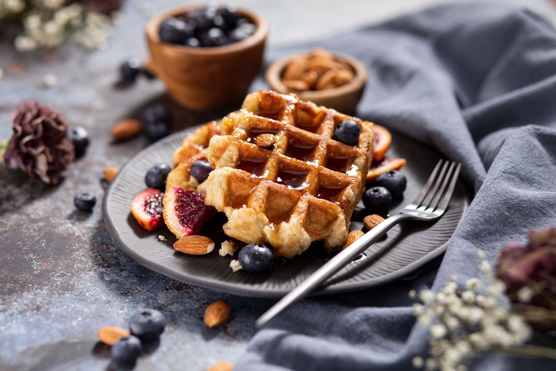 A waffle with blueberries and almonds on a plate with a fork.