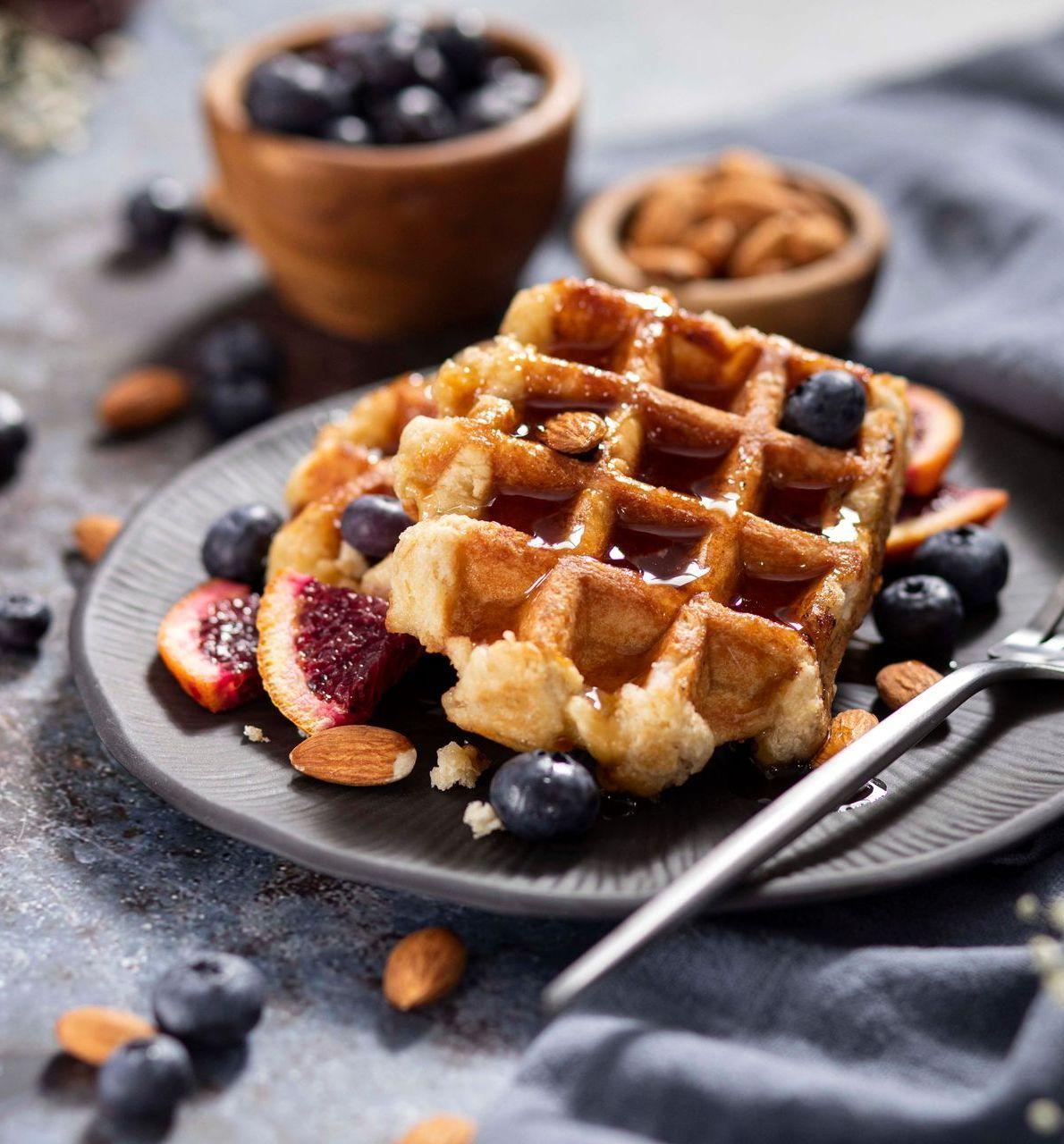 A waffle with blueberries and almonds on a plate with a fork