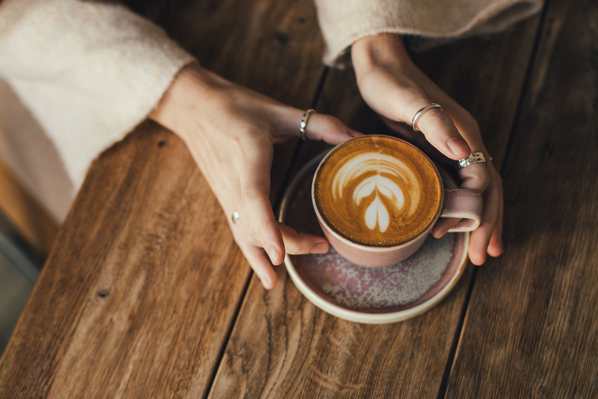 A woman is holding a cup of cappuccino on a wooden table.