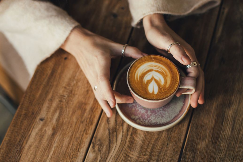 A woman is holding a cup of cappuccino on a wooden table.